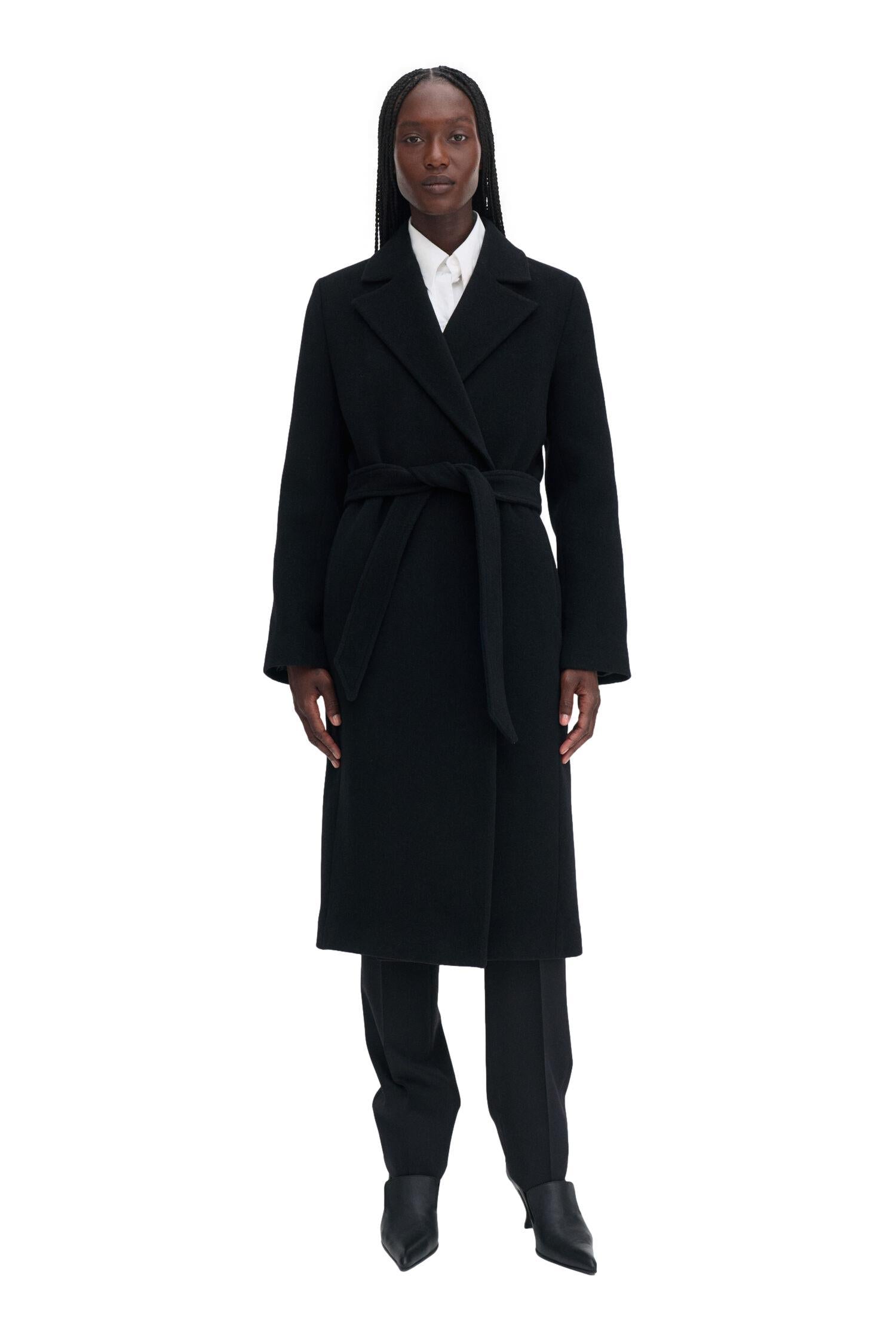 Sort Filippa K Charlotte ullkåpe med belte, lang og elegant, vist fra front med krage og knapper.