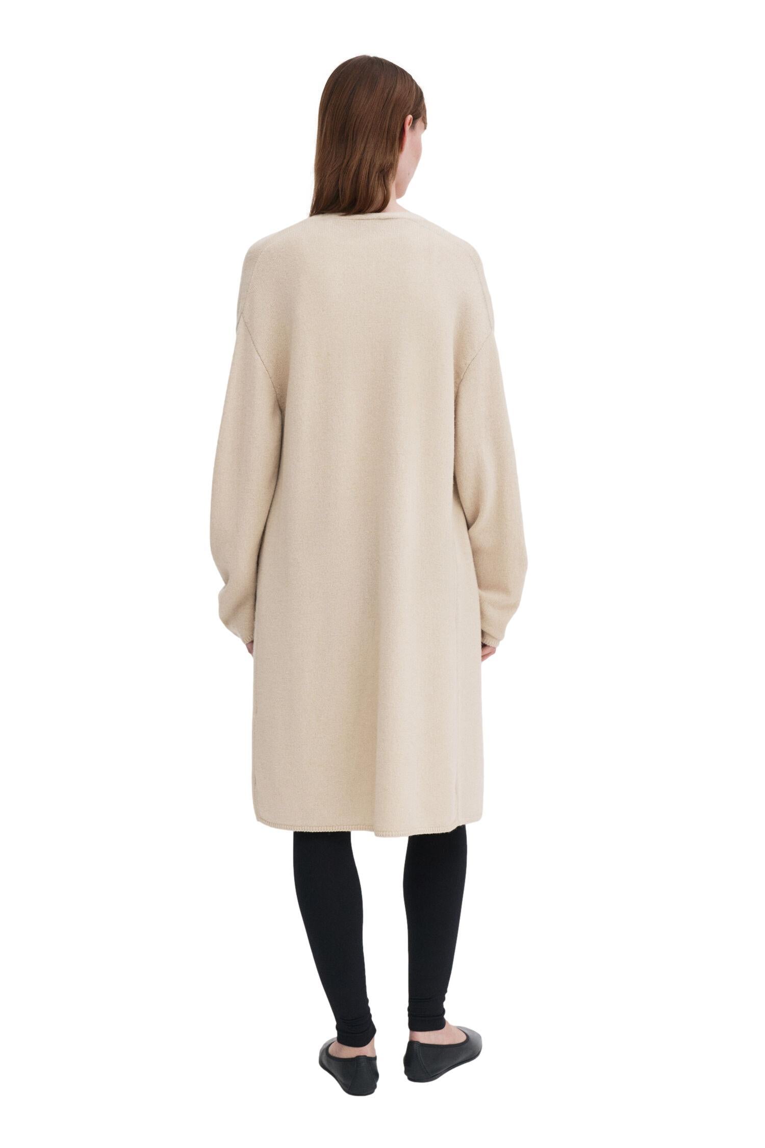 Lysebeige Filippa K ull- og kasjmirlang cardigan, myk og komfortabel, vist på en modell i et lyst rom.
